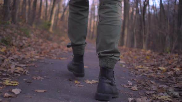 Male legs in military cargo trousers and soldier boots walks alone in forest park Low view