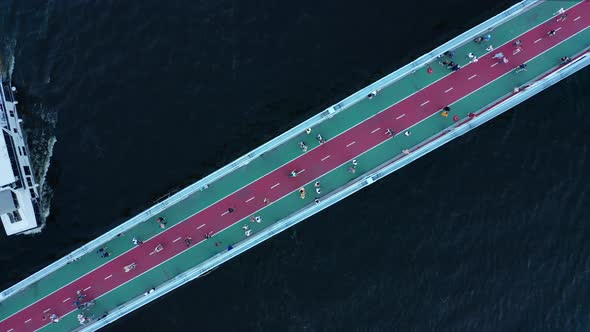 People Walk on the Pedestrian Bridge with Bike Paths Over the River with a Boat  Top Down Shot