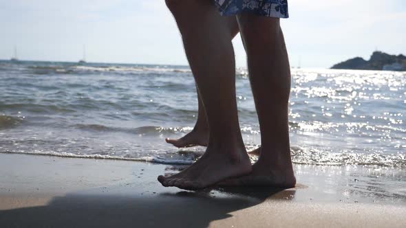 Legs of Young Couple Stepping Together Along Beach at Ocean Background