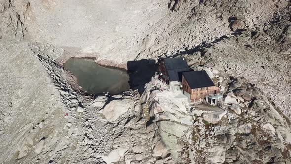 Wooden hut next to a lake for hikers and mountaineers next to rocky summits in the swiss alps, drone