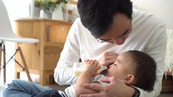 Asian Family of Young Father Feeding a Baby Boy From Milk Bottle