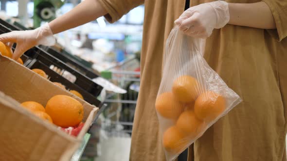 A Girl in a Supermarket Selects Fresh Oranges in Rubber Gloves and Puts Them in a Plastic Bag