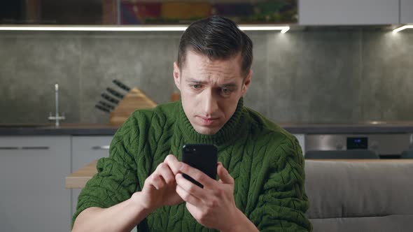 Annoyed Man Uses a Smartphone While Sitting on the Couch at Home