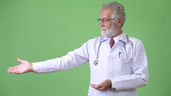 Handsome Senior Bearded Man Doctor Against Green Background