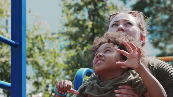 White Woman and Her Black Little Daughter Playing on the Playground Woman Helps a Girl to Reach the