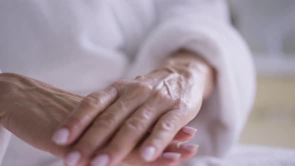 Closeup Mature Female Hands Rubbing Moisturizer in Skin Indoors