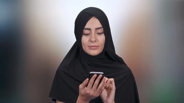 Portrait of a Young Muslim Woman, a Female in a Hijab Communicates and Uses Smartphone on a Blurred