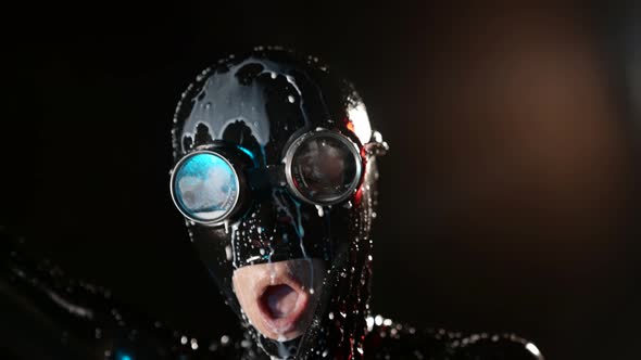 Closeup of a Head in a Black Latex Helmet and Glasses on a Dark Background