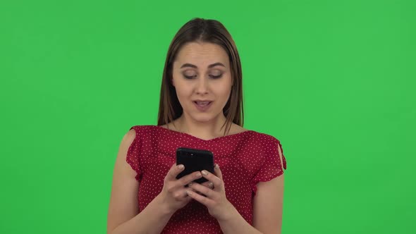 Portrait of Tender Happy Girl in Red Dress Is Texting on Her Phone. Green Screen