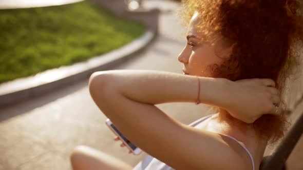 Beautiful Foxy Girl Holding Phone Relaxing Sitting on Bench Outside Slow Motion