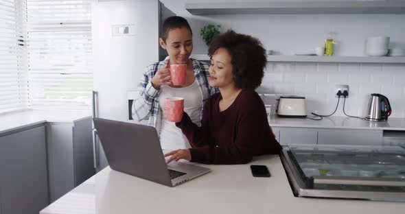 Lesbian couple having coffee and  using laptop in kitchen