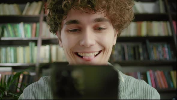 Handsome Curly Student Man Holding Modern Smartphone Texting Message in Home Office or Library alt