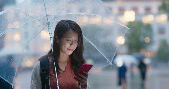 Woman use of mobile phone and hold with umbrella in the evening