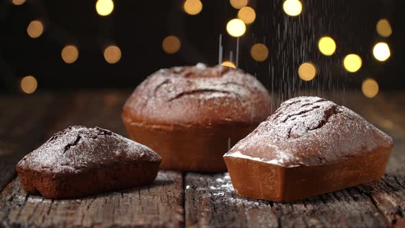 Three Christmas Breads Stollen Are Stacked on a Wooden Textured Table Sprinkled with Powdered Sugar