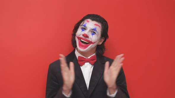 The Clown Begins the Performance in a Black Suit with Colorful Makeup on His Face Isolated on a Red