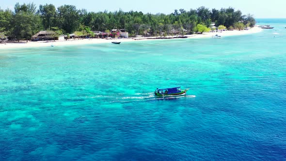 Boats sailing in the perfectly clear sea surrounding tropical island with trees and white sand beach