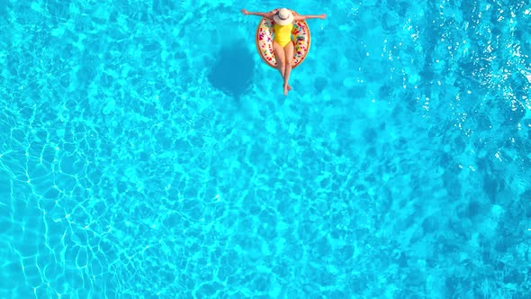 Aerial View of a Woman in Yellow Swimsuit Lying on a Donut in the Pool