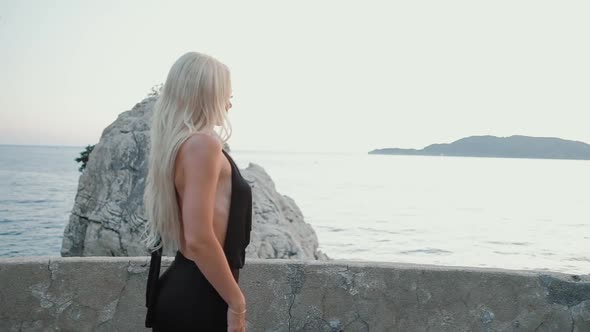 Beautiful  blonde woman  in black dress walking at sunset against the sea