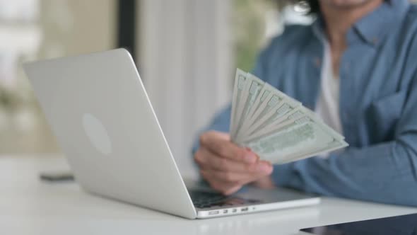 Close Up of Man Holding Dollars While Working on Laptop