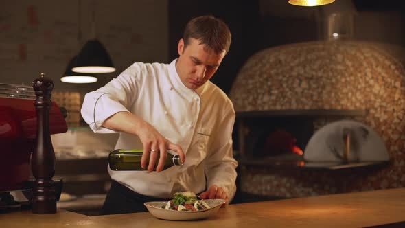 Confident Caucasian Chief Cook Pouring Olive Oil From Bottle on Tomato and Cheese Salad in Soup