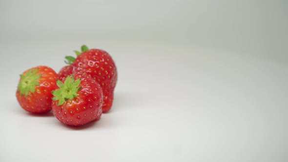 Three Red Delicious Strawberries Rotating On The Table With Pure White Background - Close Up Shot