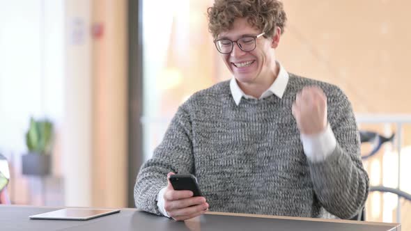 Young Man Cheering on Smartphone at Work, Success 