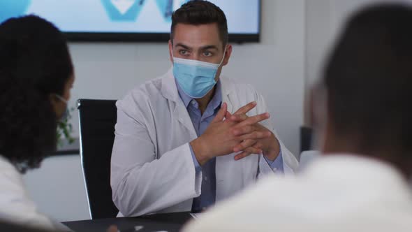 Mixed race male doctor wearing mask giving presentation in meeting room gesturing