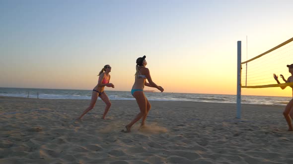 Women players play beach volleyball and celebrate a point won.