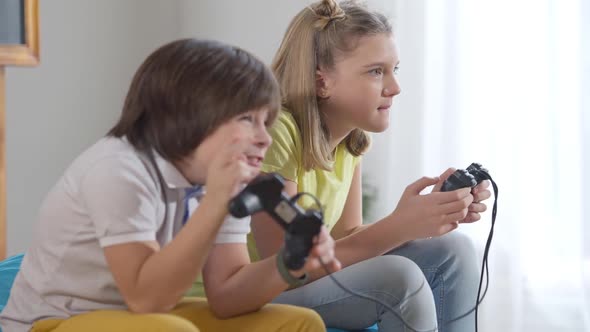 Side View Portrait of Concentrated Cheerful Caucasian Children Playing Game Console at Home