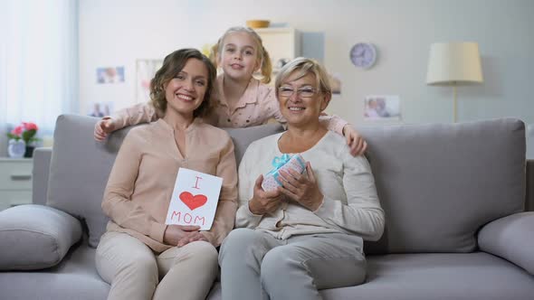 Cute Girl Hugging Mother and Granny With Present Box and Hand-Made Greeting Card