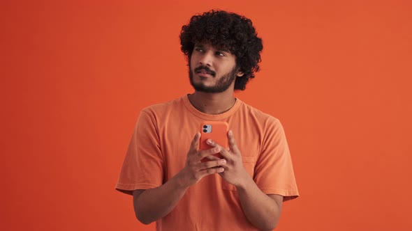 Cheerful curly-haired Indian man looking at the phone
