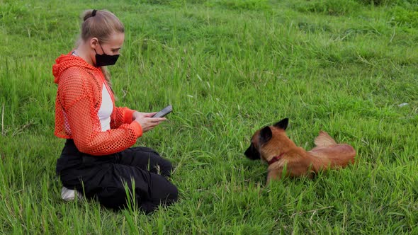 A Young Blonde Woman with a Braid Wearing an Orange Hoodie with a Mask on Her Face Plays on the