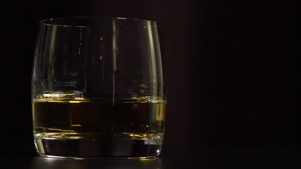 A Man Lifts a Glass of Whiskey From a Table - Closeup - Dark Background