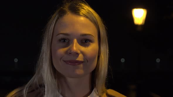 A Young Beautiful Woman Smiles at the Camera in an Urban Area at Night - Closeup