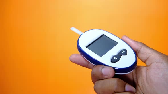 Hand Holding Blood Glucose Meters on Orange Background 