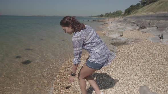 Close Up Shot Of Young Woman Reaching Down To Pick Up Plastic Bottle On Beach In Slowmotion