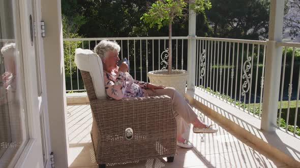 Caucasian senior woman drinking coffee while sitting on a chair in the balcony at home