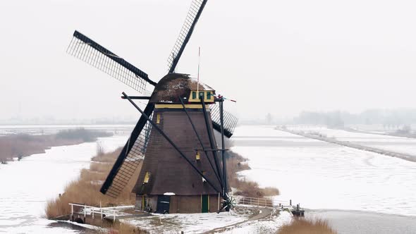 Line of old world heritage Kinderdijk windmills with front spinning by icy canal