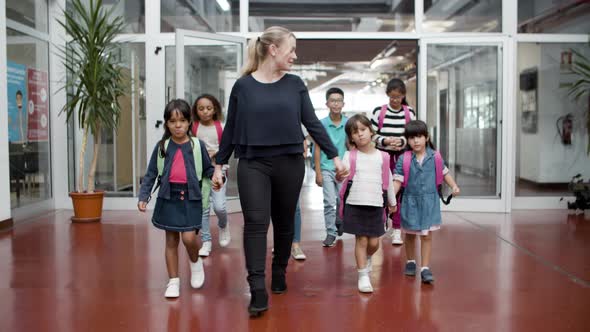 Multiethnic Schoolkids Walking in Hallway with Female Tutor