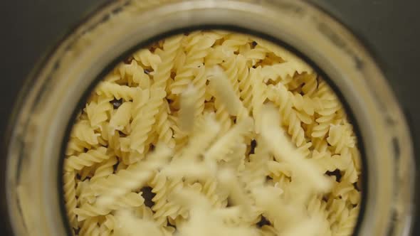 TOP VIEW: Uncooked Spiral Pasta Fall Into Glass Jar On Black Background - Slow Motion