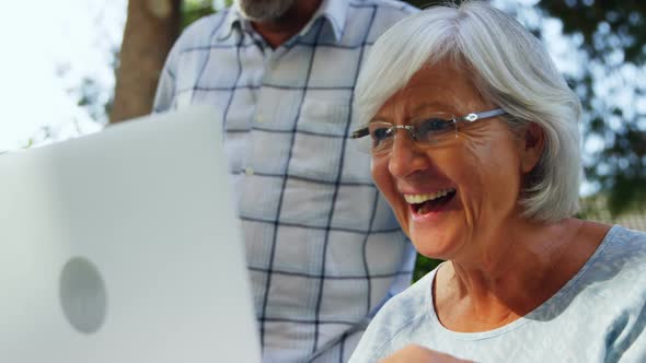 Happy senior woman using laptop in garden 4k