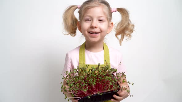 A Small Blonde Girl Smiles and Holds a Seedling of Micro Greens in Her Hands