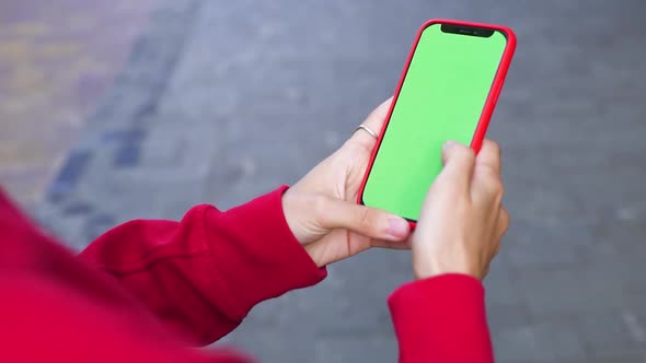 Close-up of Woman Arms in Red Sweater Holding Green Screen Phone on the Street