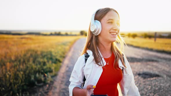 Young Girl Stands on Country Road in Field and Uses Her Phone to Switch Songs in Her Headphones
