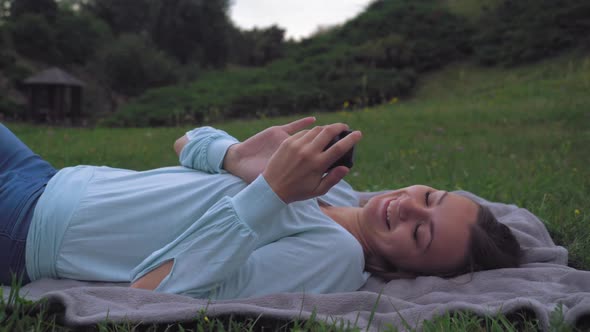 Young Girl Lying on the Lawn in the Park, Gaining a Message on Your Phone, Then Closes His Eyes