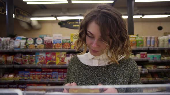 Young Curly Haired Woman Doing Grocery Shopping at the Supermarket She is Reading a Product Label