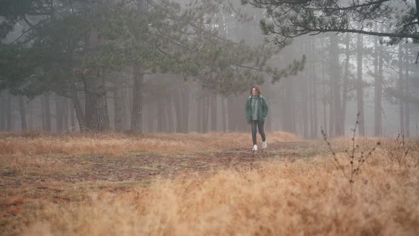 A Young Woman with a Backpack Walking Along a Path in the Misty Forest