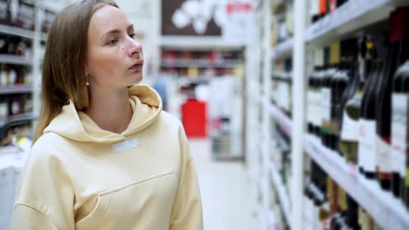 Woman Chooses Wine in the Supermarket, Customer Selects Product on the Shelves in the Store