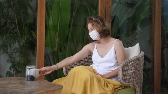 Sick Young Woman in Protective Mask Daydreaming and Drinking Tea on Terrace While Quarantining