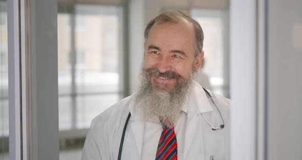 Portrait of Confident Senior Doctor Looking Through Window and Smiling